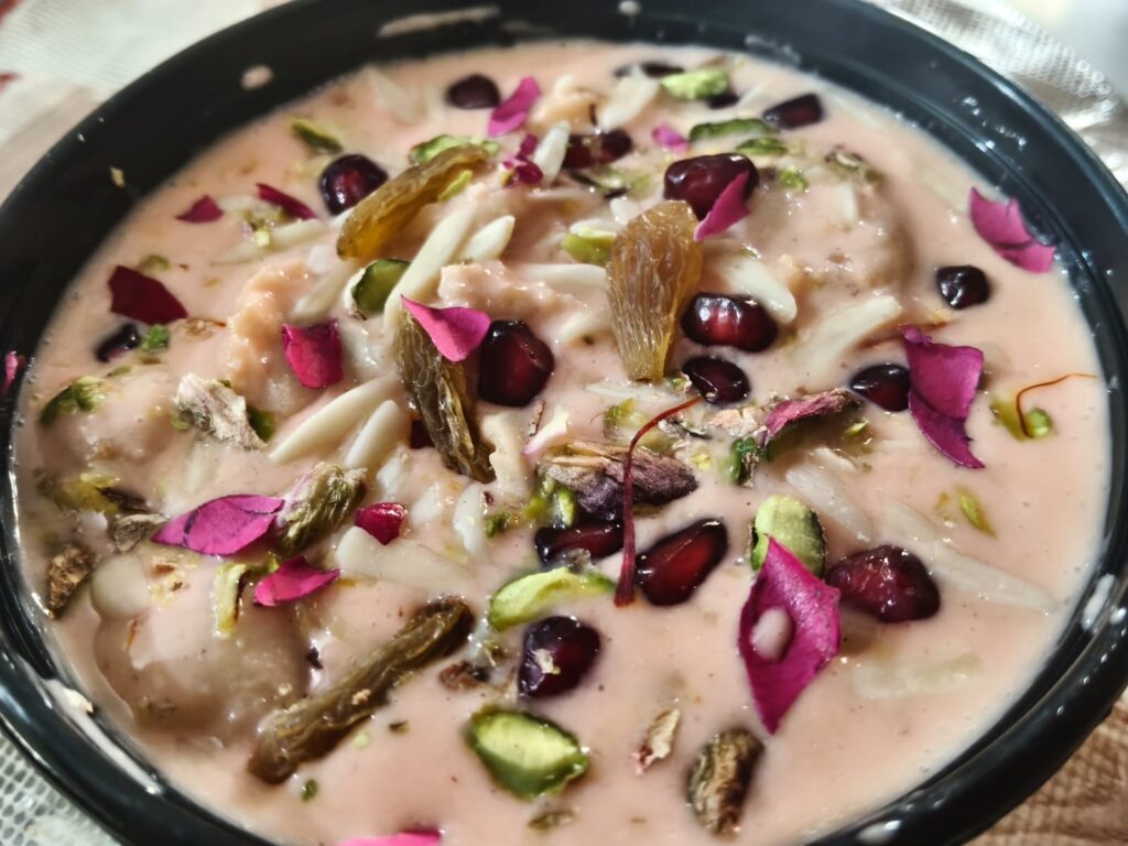 Creamy dahi bhalla plate topped with fresh pomegranate, raisins, nuts, and rose petals.