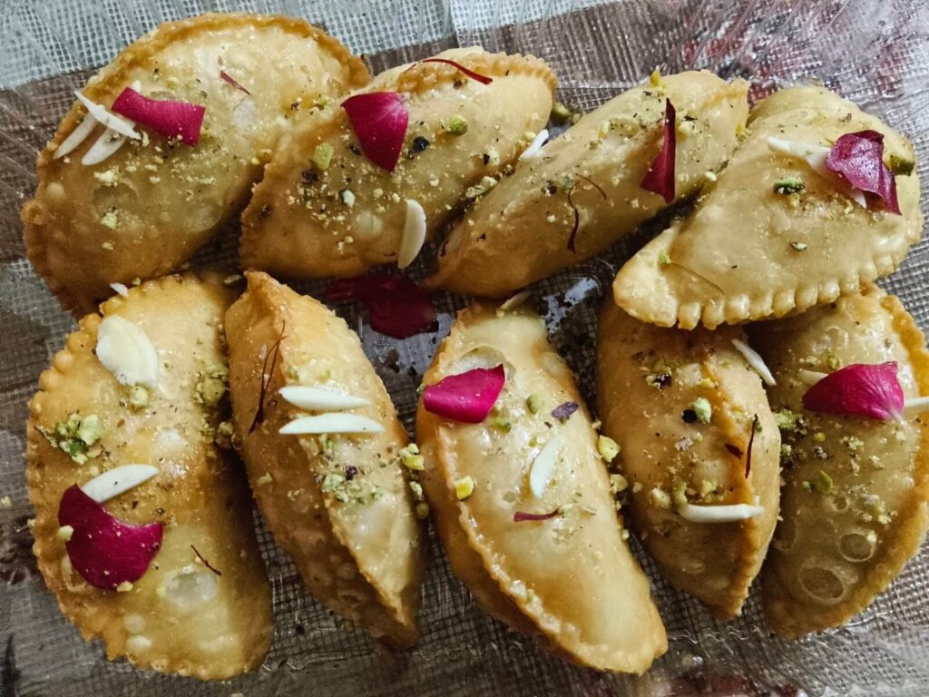 Traditional Gujiya sweet stuffed with dry fruit mawa and garnished with almonds, pistachios, and rose petals.