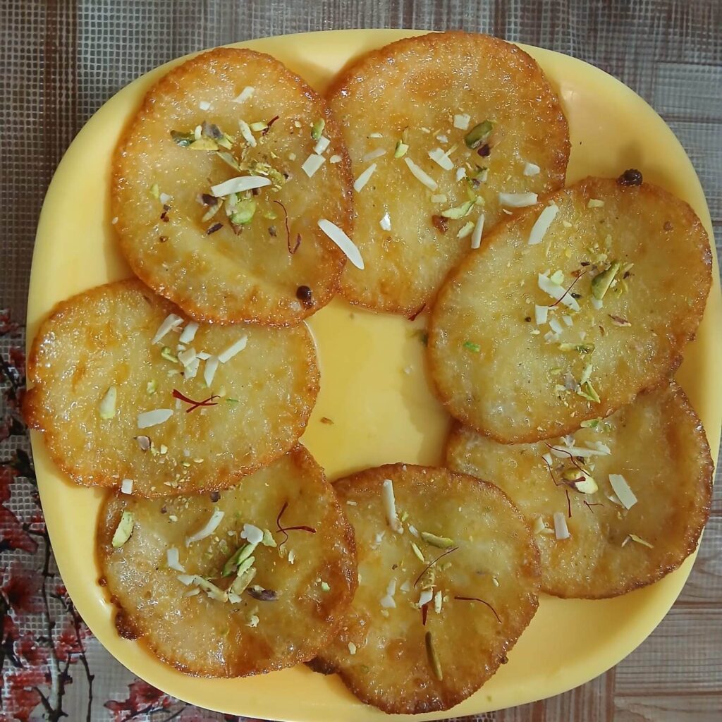 Fresh desi ghee malpua topped with pistachios, almonds, and saffron served on a yellow plate